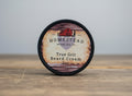 Homestead Beard Oil Co. True Grit Beard Cream container on a field background