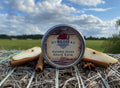 Homestead Beard Oil Co. Autumn Grove Beard Balm container on a natural background with a cloudy sky.