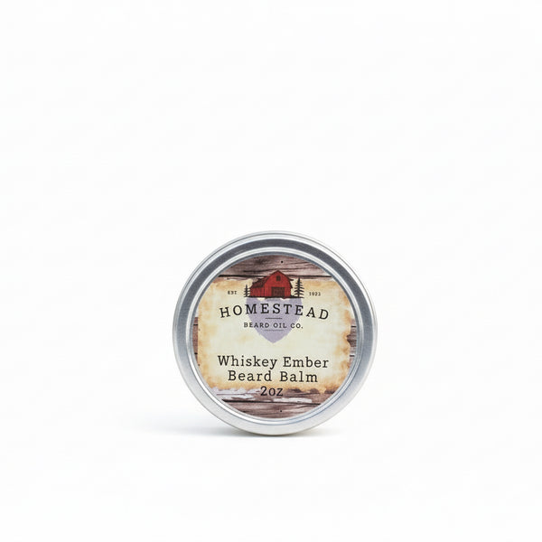 Homestead Herbs & Oil Co. Whiskey Ember Beard Balm container on a grassy field with a blue sky.