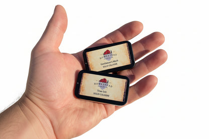 Two solid cologne tins held in a hand against a natural white background
