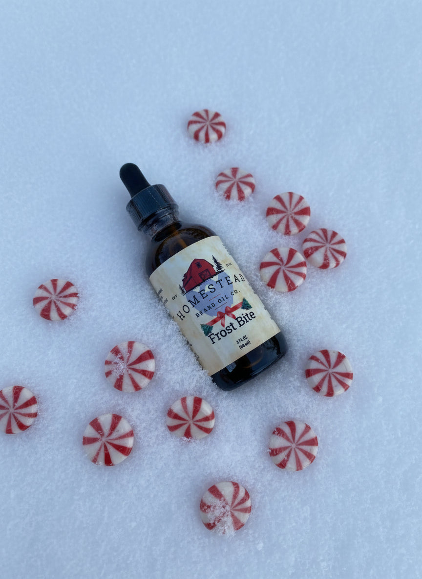 Bottle of Homestead Beard Oil Co. laying in the snow, surrounded by peppermints with a natural background
